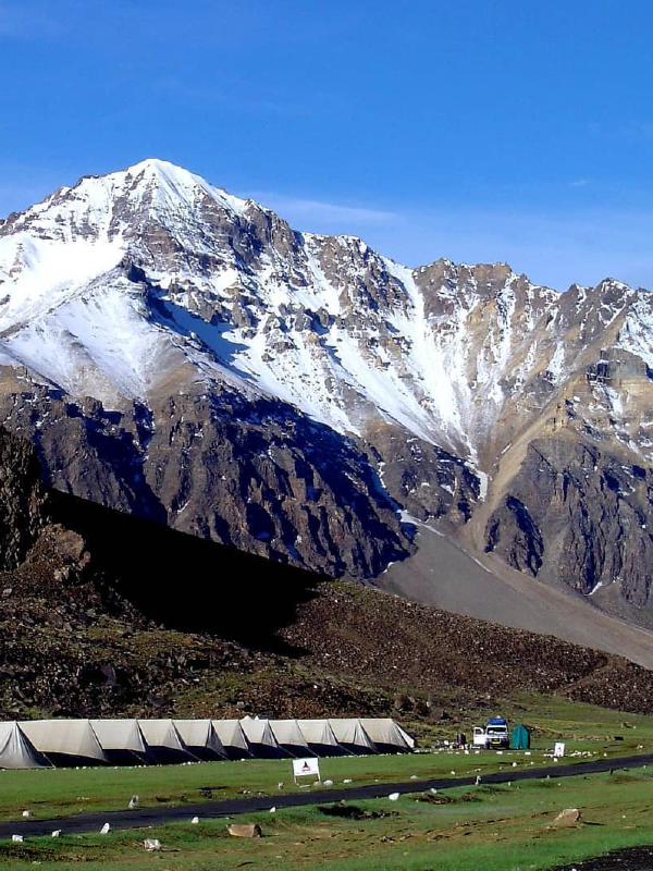 "A scenic view of the verdant fields and scattered houses in the valley of Leh-Ladakh, with barren mountains rising in the background under a partly cloudy sky."